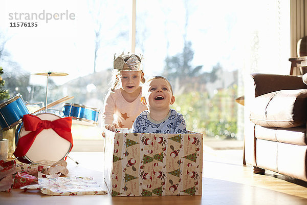 Mädchen schiebt Bruder in Pappkarton zu Weihnachten