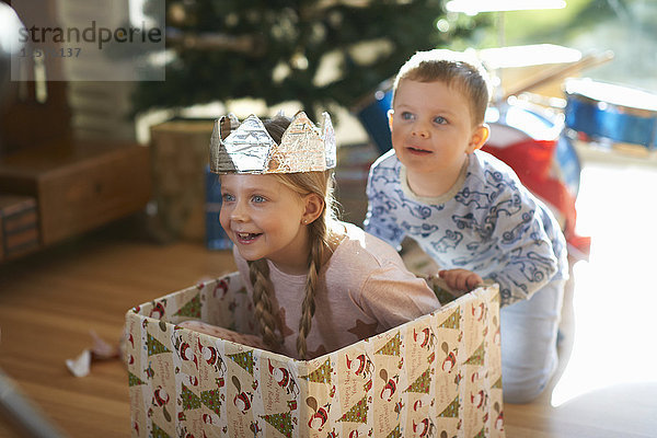 Junge schiebt Schwester in Pappkarton zu Weihnachten