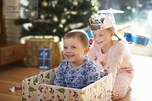 Mädchen schiebt Bruder in Pappkarton zu Weihnachten