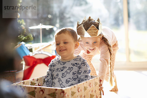 Mädchen schiebt Bruder in Pappkarton zu Weihnachten