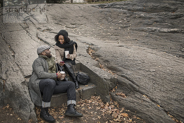 Ehepaar sitzt auf einer Treppe im Park mit Kaffee zum Mitnehmen