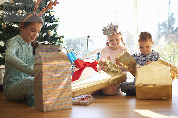 Junge und Schwestern sitzen auf dem Wohnzimmerboden und öffnen Weihnachtsgeschenke