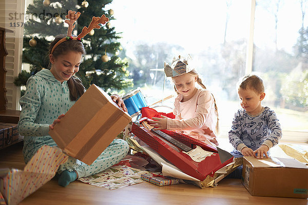 Junge und Schwestern sitzen auf dem Wohnzimmerboden und öffnen Weihnachtsgeschenke