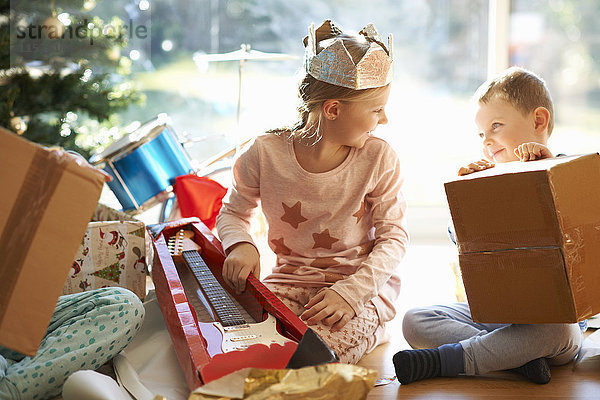 Junge und Schwester sitzen auf dem Wohnzimmerboden und öffnen Weihnachtsgeschenke