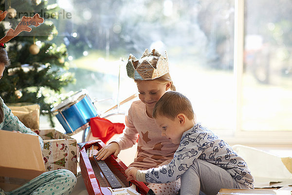 Mädchen und Bruder auf dem Wohnzimmerboden betrachten Spielzeuggitarre als Weihnachtsgeschenk