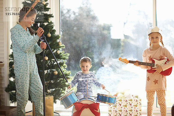 Junge und Schwestern spielen Spielzeug-Schlagzeug und Gitarre am Weihnachtstag