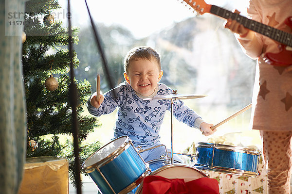 Junge und Schwester spielen am Weihnachtstag Spielzeug-Schlagzeug und Gitarre