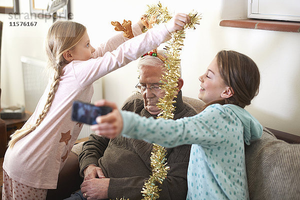 Schwestern nehmen Smartphone-Selfie  während sie Lametta auf den schlafenden Großvater legen