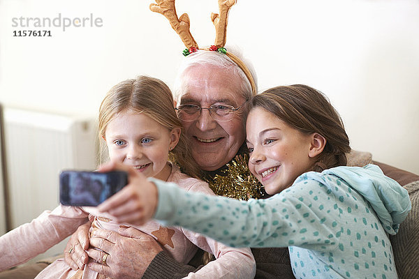 Schwestern beim Smartphone-Selfie mit Großvater im Rentiergeweih