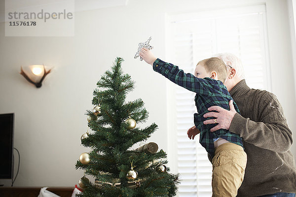 Älterer Mann hebt Enkel hoch  um Stern auf Weihnachtsbaum zu setzen