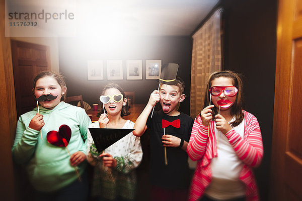 Porträt eines Jungen und dreier Mädchen mit Sonnenbrille und Schnurrbartstockmasken auf einer Party