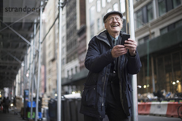 Mann lehnt an Laternenpfahl und hält Smartphone lachend  Manhattan  New York  USA