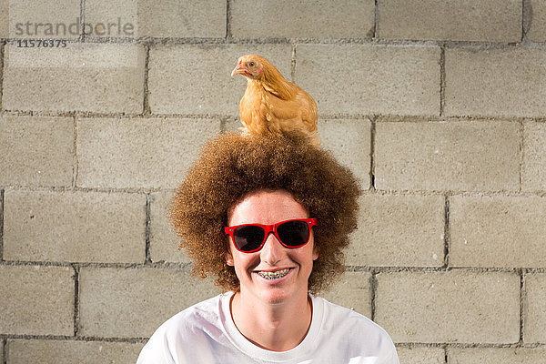 Porträt eines Teenagers mit roten Afrohaaren  Huhn auf dem Kopf sitzend