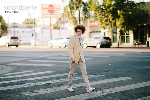 Teenager-Junge mit roten Afrohaaren  im Anzug  auf einem Fußgängerüberweg