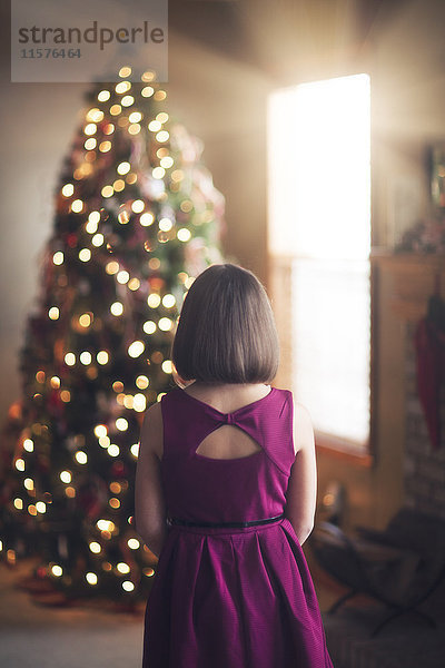 Junges Mädchen betrachtet geschmückten Weihnachtsbaum  Rückansicht