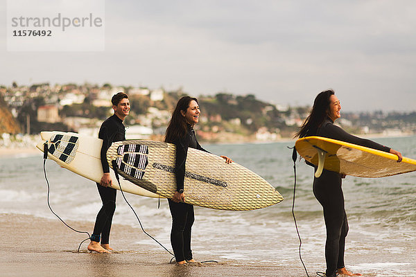 Drei Freunde stehen im Meer  halten Surfbretter in der Hand und bereiten sich auf das Surfen vor