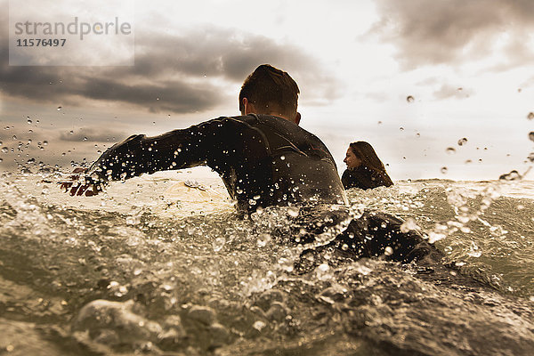 Zwei Freunde im Meer  paddeln auf Surfbrettern  Rückansicht