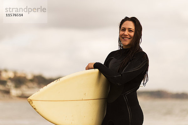 Junge Frau  die vom Meer weggeht und Surfbretter trägt