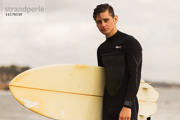 Porträt eines jungen Mannes  der ein Surfbrett hält