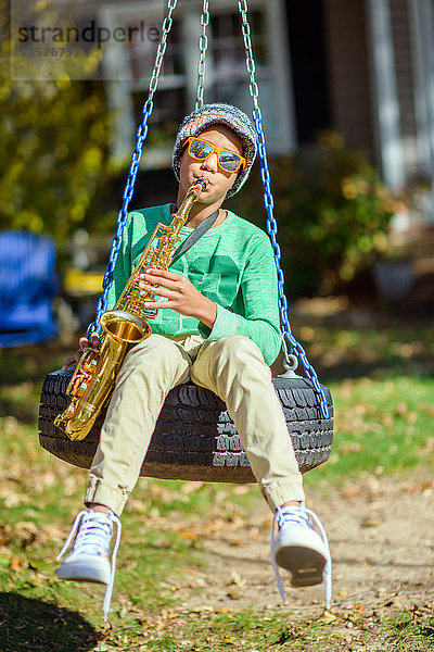 Teenager  sitzt auf Reifenschaukel  spielt Saxophon