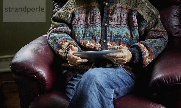 Ältere Frau auf Stuhl sitzend  hält digitales Tablet  Mittelteil