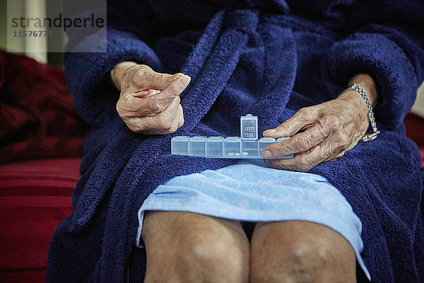 Ältere Frau sitzt auf der Bettkante und nimmt Tabletten vom Pillenorganisator  Mittelteil
