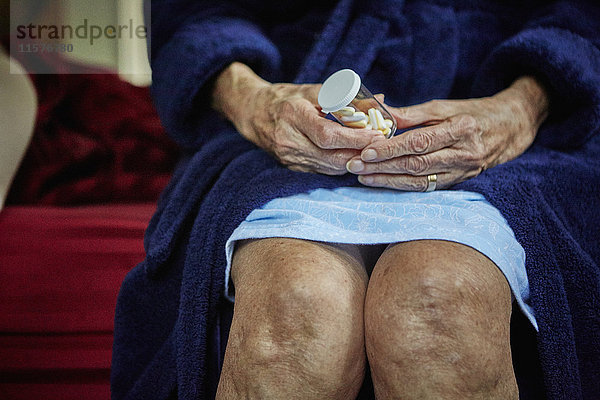 Ältere Frau sitzt auf der Bettkante  hält Tablettenfläschchen  Mittelteil