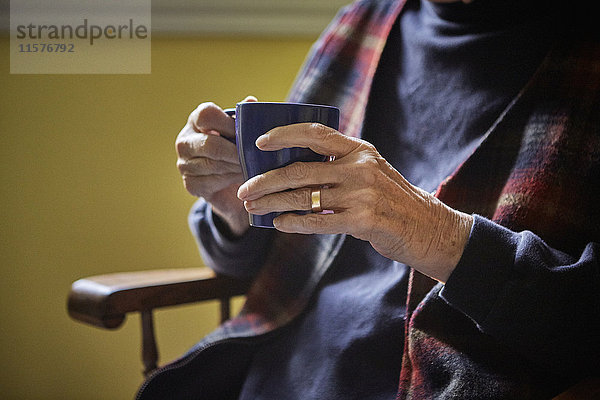 Ältere Frau auf dem Stuhl sitzend  heißes Getränk in der Hand  Mittelteil