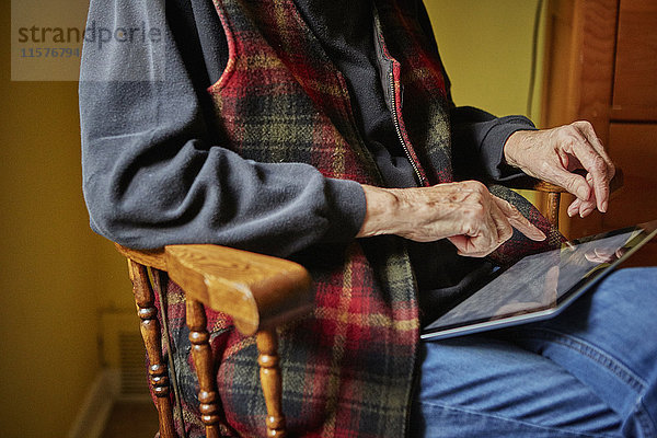 Ältere Frau auf Stuhl sitzend  mit digitalem Tablett  Mittelteil