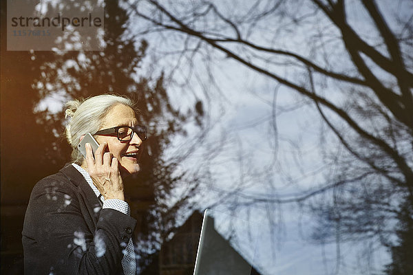 Ansicht des Hauptfensters einer älteren Geschäftsfrau  die einen Smartphone-Anruf tätigt