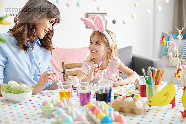 Mädchen und Mutter bemalen Ostereier bei Tisch