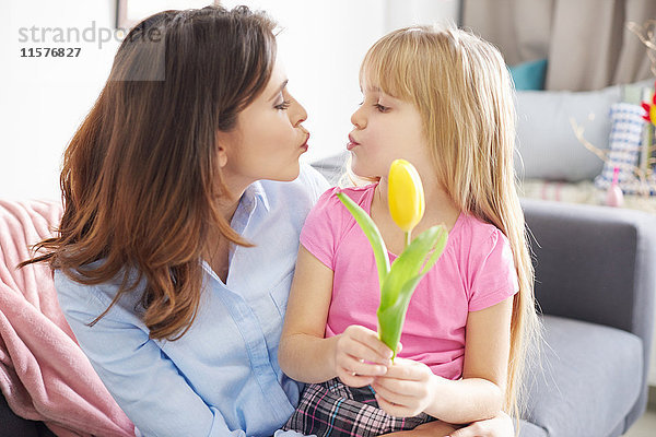 Mädchen  das der Mutter eine Tulpe reicht und auf dem Sofa die Lippen kräuselt