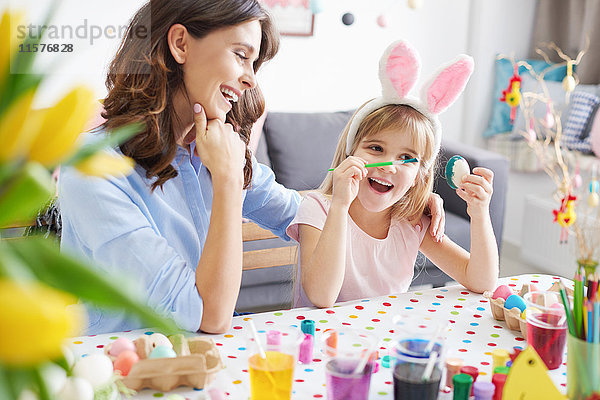 Frau und Tochter malen Ostereier bei Tisch