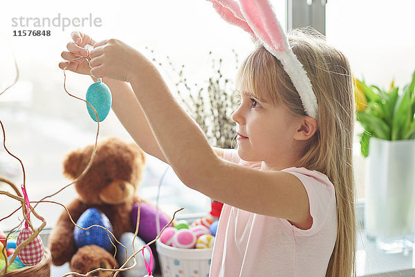 Mädchen in Hasenohren macht Ostereierschmuck im Wohnzimmer