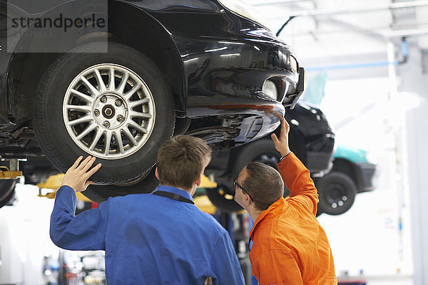 Rückansicht von Mechaniker-Studenten  die die Unterseite eines Autos inspizieren