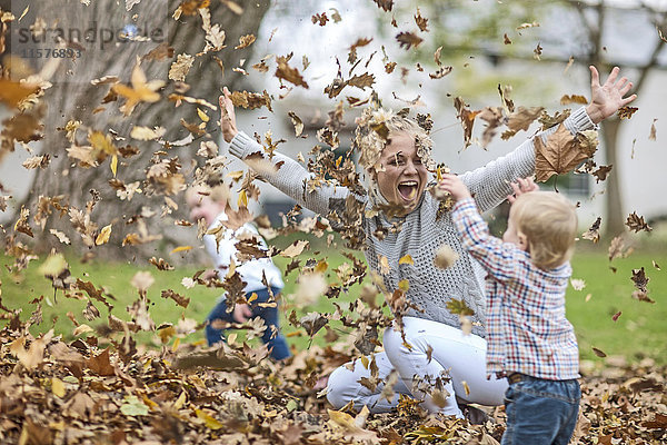 Mutter und Kinder spielen mit heruntergefallenen Blättern