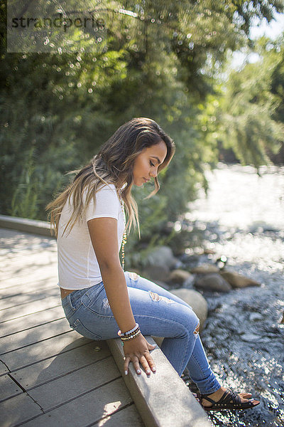 Teenager-Mädchen sitzt auf Fußgängerbrücke und starrt auf Fluss