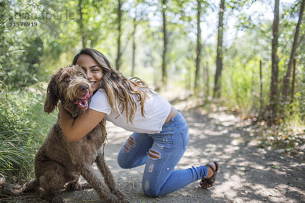 Porträt eines Teenager-Mädchens  das einen süßen Hund auf einem Waldweg umarmt