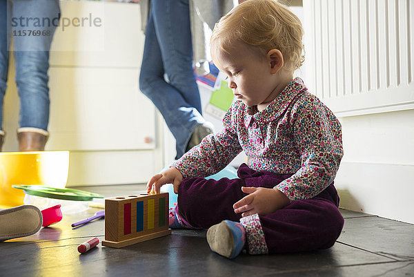 Kleines Mädchen sitzt auf dem Küchenboden und spielt mit Spielzeug