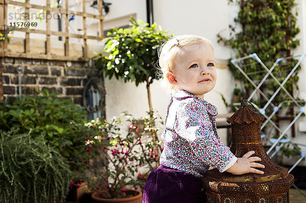 Kleines Mädchen stehend und lehnend an der Gartenlaterne