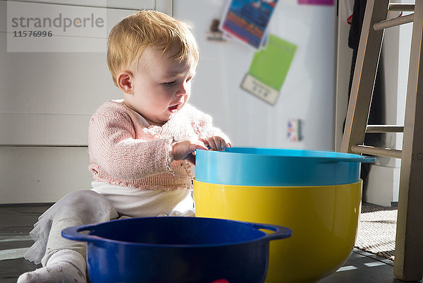 Kleines Mädchen sitzt auf dem Küchenboden und spielt mit Schüsseln