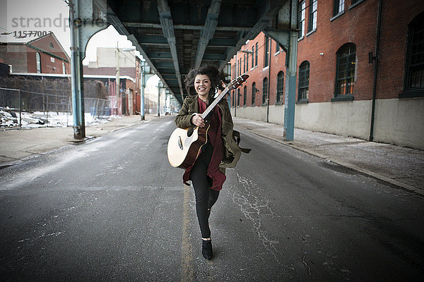 Junge Frau läuft mit Akustikgitarre unter einer Hochstraße