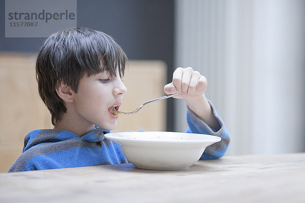 Junge isst sein Mittagessen aus einer Schüssel am Küchentisch