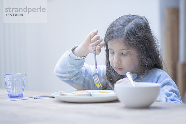 Mädchen isst pochiertes Eierfrühstück am Küchentisch