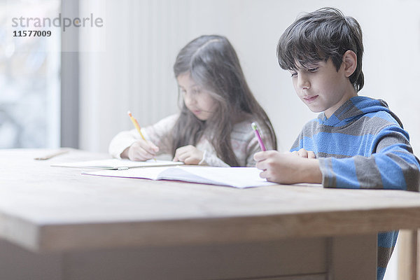 Junge und Schwester machen Hausaufgaben am Küchentisch