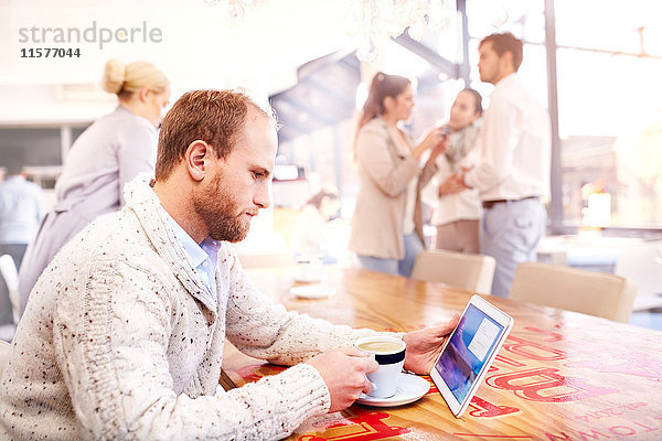 Junger Mann allein im Café mit Blick auf digitales Tablet