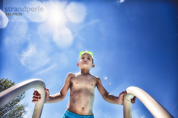 Niedrigwinkel-Ansicht eines Jungen auf einer Schwimmbadleiter gegen blauen Himmel