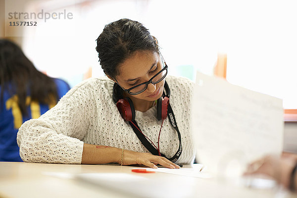 Junge Studentin schreibt am Schreibtisch im College-Klassenzimmer