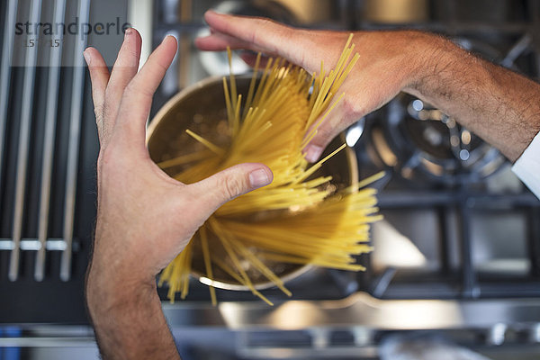 Koch  der Spaghetti in einem Kochtopf auf den Herd stellt  Nahaufnahme  Draufsicht