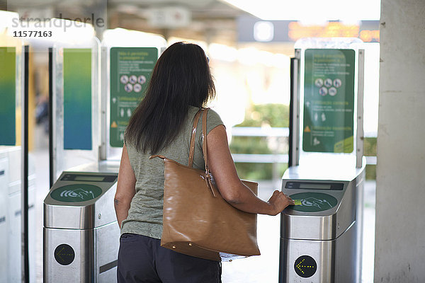 Rückansicht einer Frau  die den Touchscreen der Fahrkarte an der Bahnschranke benutzt